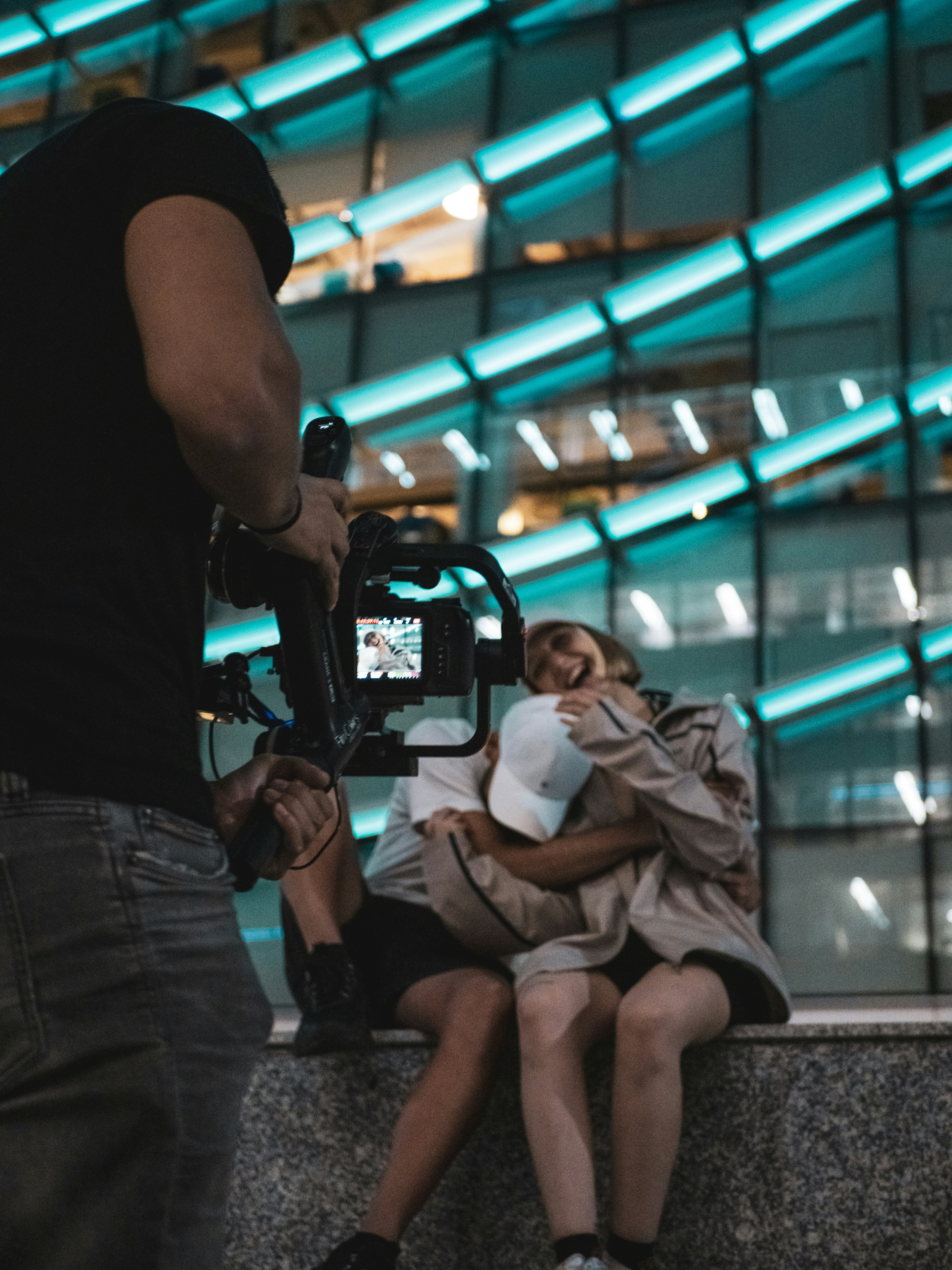 man in black t-shirt and gray shorts sitting on gray concrete bench holding black smartphone